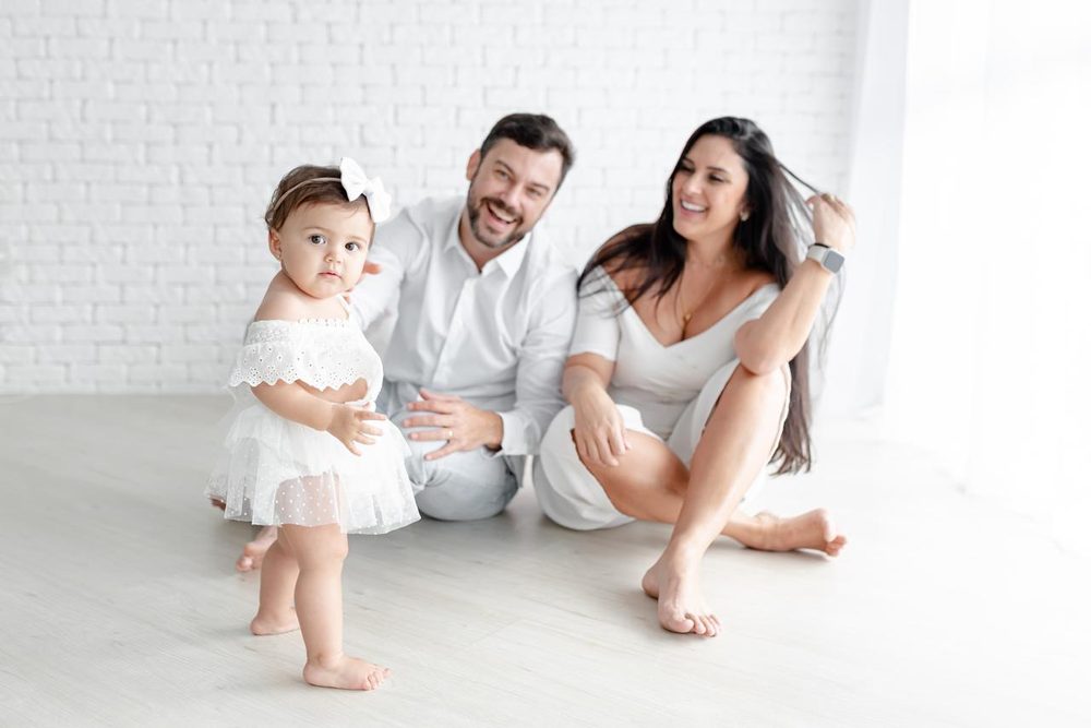 Família sorrindo com a bebê dando os primeiros passos